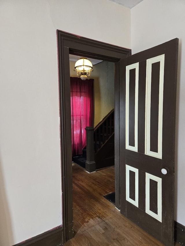 corridor with a notable chandelier, hardwood / wood-style flooring, and stairs