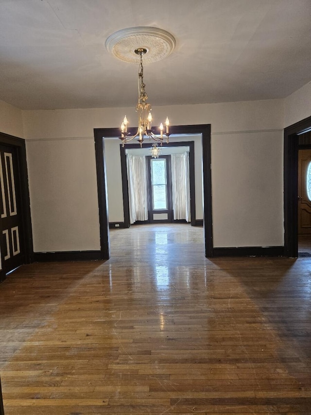 unfurnished dining area featuring wood finished floors, an inviting chandelier, and baseboards