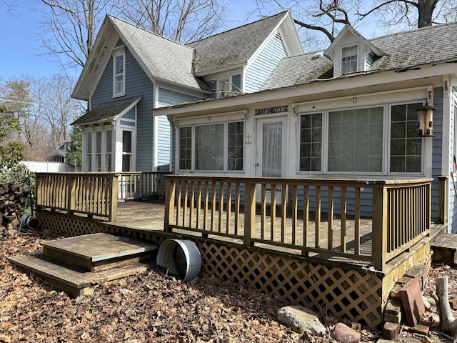 back of property with a wooden deck, a sunroom, and a shingled roof