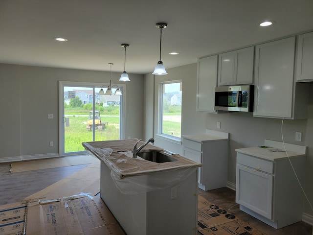 kitchen with an island with sink, hanging light fixtures, light stone countertops, white cabinets, and sink