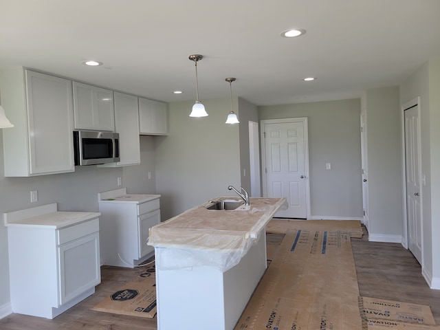 kitchen with pendant lighting, light hardwood / wood-style flooring, white cabinetry, sink, and a center island with sink