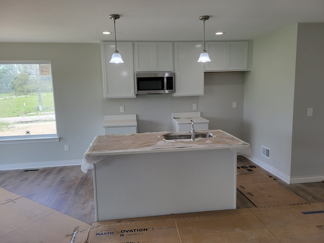 kitchen featuring decorative light fixtures, white cabinets, and an island with sink