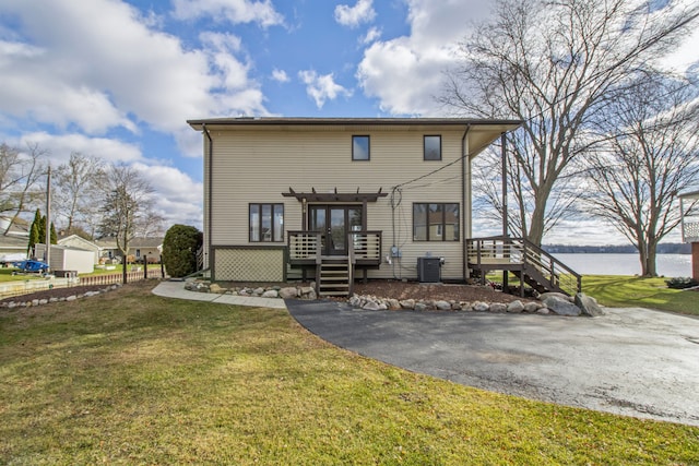 rear view of property with cooling unit, a yard, and a deck with water view