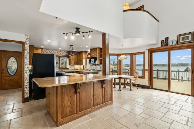 kitchen with light stone countertops, a center island, a high ceiling, pendant lighting, and a water view