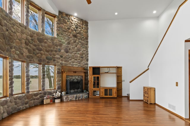 unfurnished living room featuring wood-type flooring, a stone fireplace, and ceiling fan