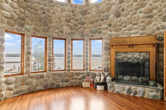 unfurnished living room with a stone fireplace, a water view, and hardwood / wood-style flooring