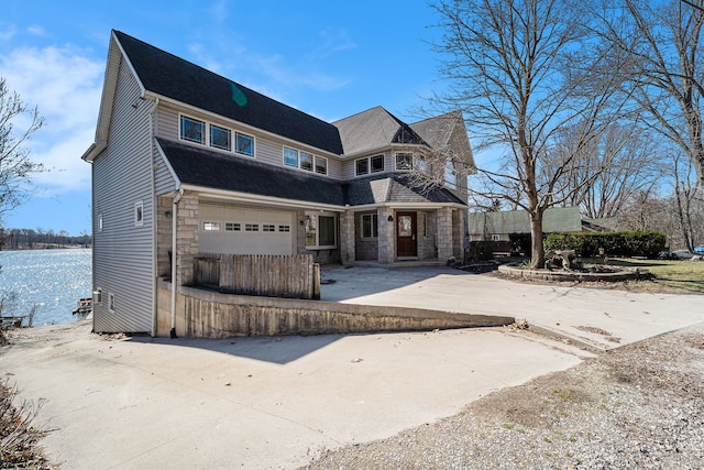 shingle-style home featuring an attached garage, stone siding, and concrete driveway