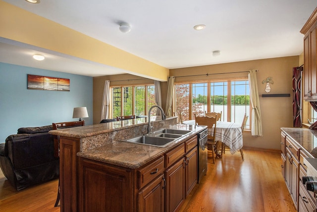 kitchen featuring sink, stainless steel dishwasher, light hardwood / wood-style floors, a breakfast bar, and a center island with sink