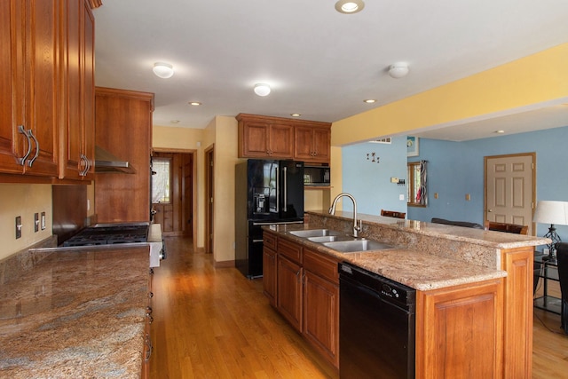 kitchen with sink, a kitchen bar, a center island with sink, black appliances, and light wood-type flooring