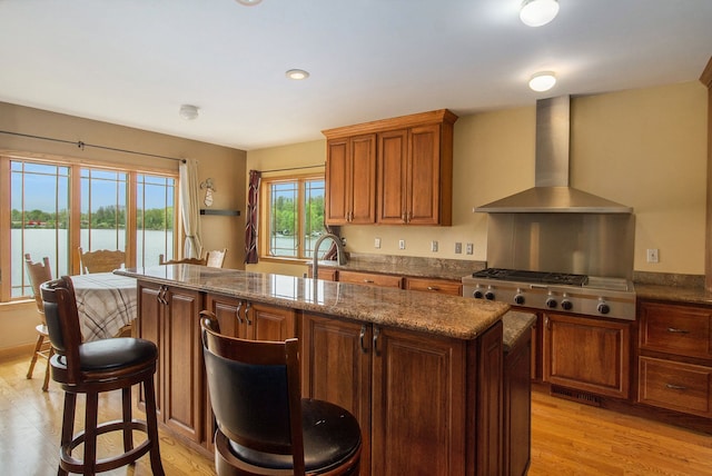 kitchen featuring stainless steel gas stovetop, light wood-type flooring, wall chimney range hood, and a water view