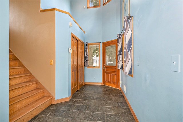 foyer featuring visible vents, a towering ceiling, stairway, stone finish floor, and baseboards