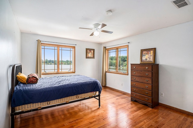 bedroom with ceiling fan, light hardwood / wood-style floors, and a water view