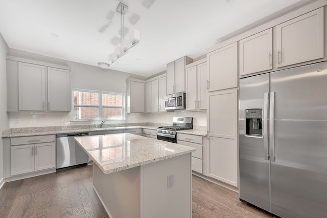 kitchen with a center island, dark wood-type flooring, sink, light stone counters, and stainless steel appliances