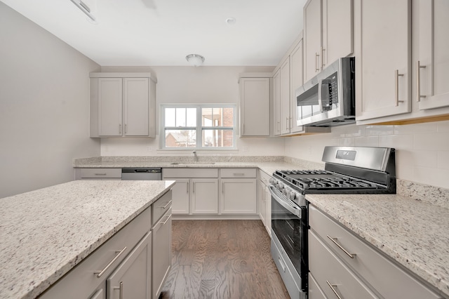 kitchen featuring appliances with stainless steel finishes, light wood-type flooring, tasteful backsplash, light stone counters, and sink