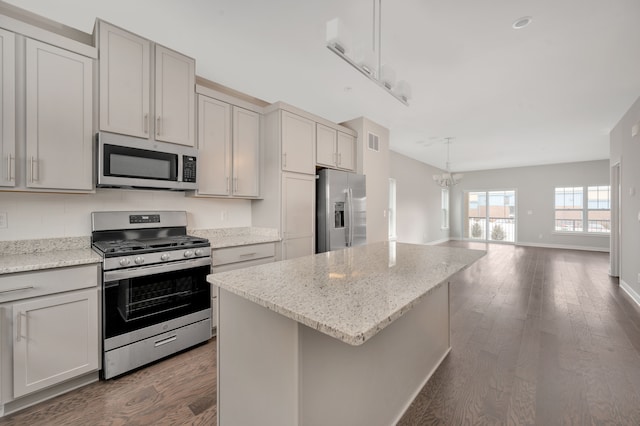 kitchen with light stone countertops, hanging light fixtures, dark wood-type flooring, a kitchen island, and appliances with stainless steel finishes