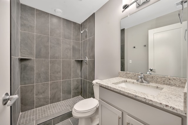 bathroom with a tile shower, vanity, toilet, and tile patterned floors