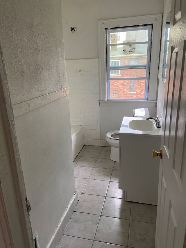 bathroom featuring tile patterned floors, a tub to relax in, toilet, vanity, and tile walls