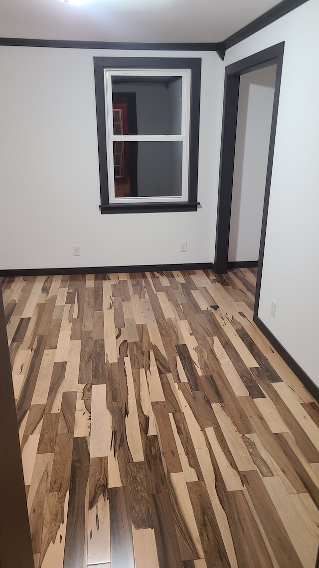 empty room with hardwood / wood-style flooring and crown molding