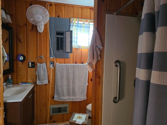 bathroom featuring electric panel, wood walls, heating unit, toilet, and vanity