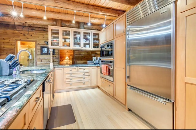 kitchen with beam ceiling, wooden ceiling, built in appliances, dark stone countertops, and light brown cabinetry