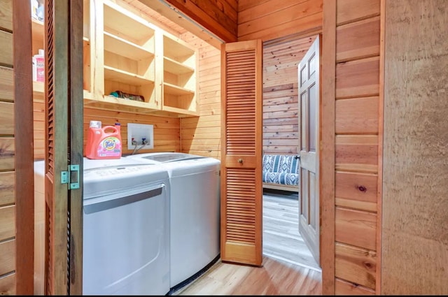 clothes washing area with washer and clothes dryer, wood walls, and light hardwood / wood-style flooring