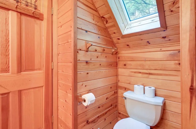 bathroom featuring lofted ceiling with skylight, wood walls, and toilet