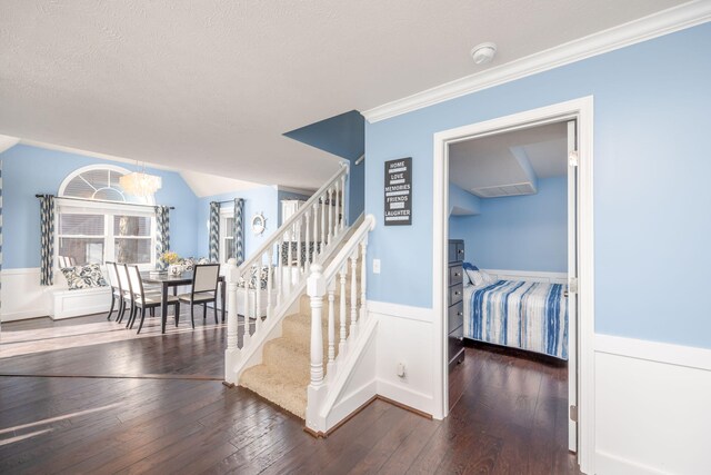 stairway featuring a chandelier, wood-type flooring, a textured ceiling, and ornamental molding