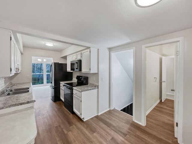 kitchen with hardwood / wood-style floors, white cabinetry, sink, and black appliances