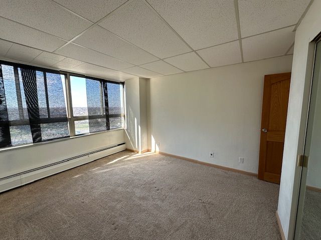 carpeted empty room featuring a water view, a drop ceiling, and a baseboard heating unit