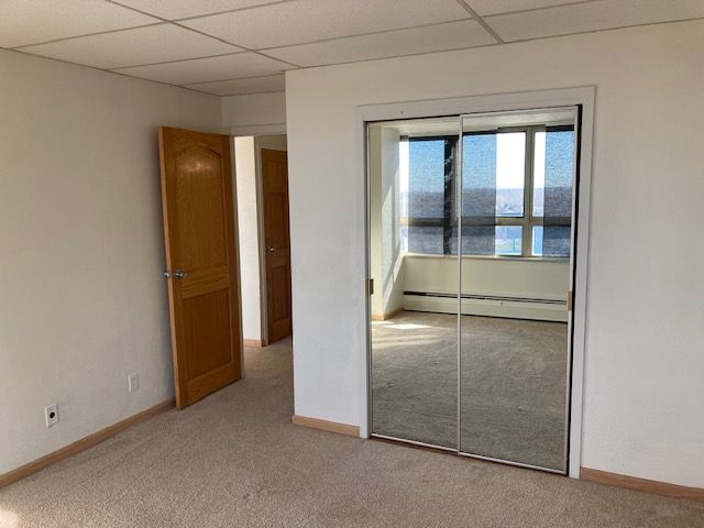 unfurnished bedroom featuring light carpet, a paneled ceiling, a baseboard radiator, and a closet