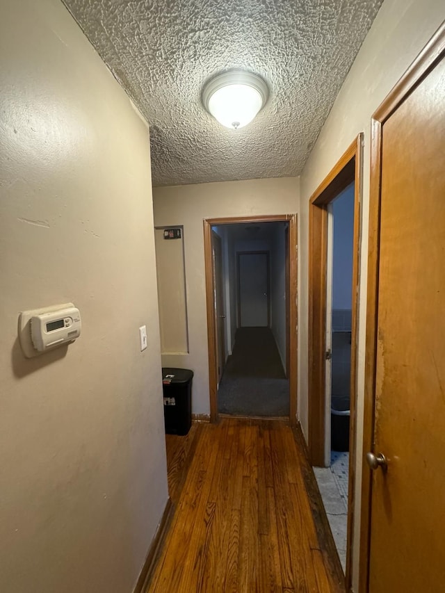 hallway with a textured ceiling and dark hardwood / wood-style flooring