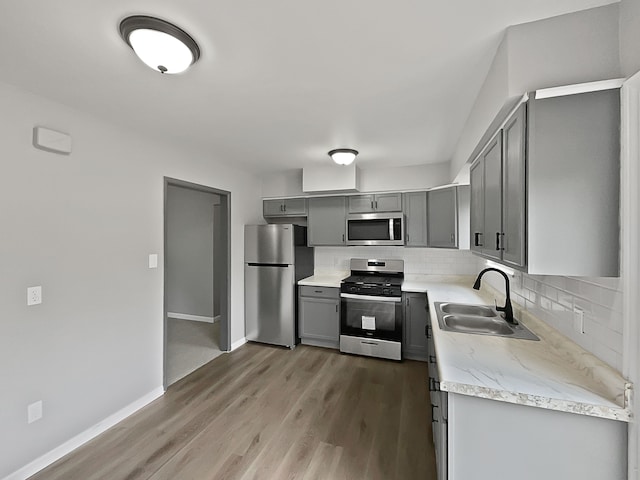 kitchen featuring gray cabinetry, backsplash, sink, appliances with stainless steel finishes, and wood-type flooring