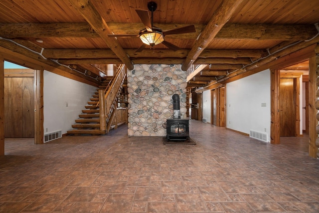 unfurnished living room with beamed ceiling, ceiling fan, a wood stove, and wood ceiling