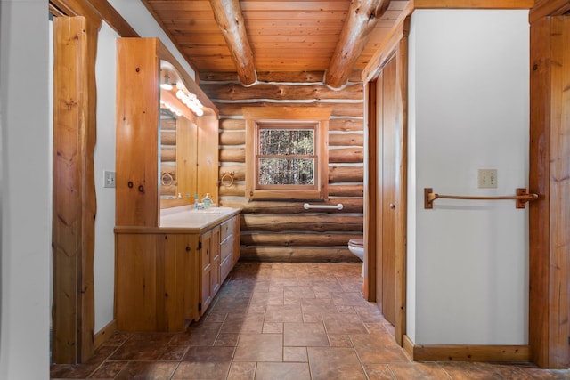 bathroom featuring rustic walls, wood ceiling, vanity, beamed ceiling, and toilet