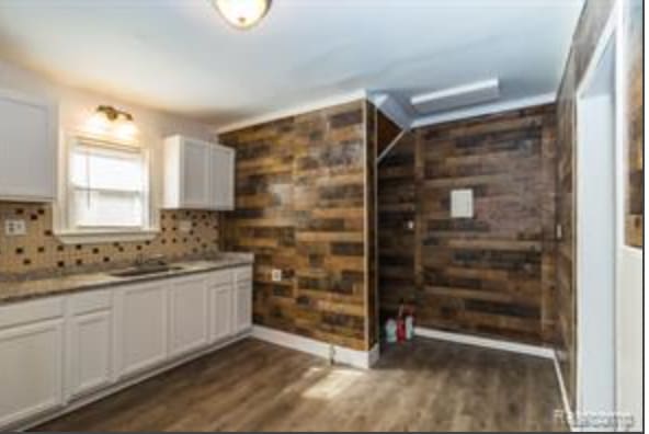 kitchen with dark hardwood / wood-style flooring, tasteful backsplash, wooden walls, sink, and white cabinetry