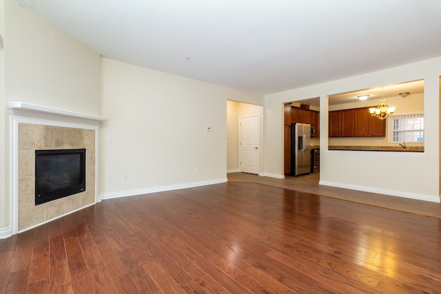 unfurnished living room with a tiled fireplace, sink, dark hardwood / wood-style floors, and an inviting chandelier