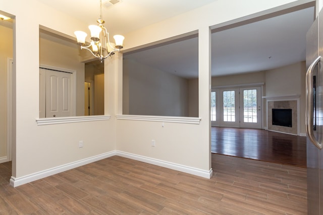 unfurnished dining area with a tiled fireplace, wood-type flooring, french doors, and a chandelier