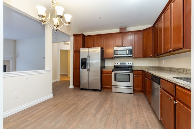 kitchen with appliances with stainless steel finishes, light stone counters, an inviting chandelier, light hardwood / wood-style flooring, and hanging light fixtures