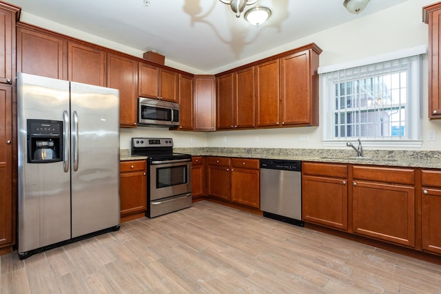 kitchen featuring light stone countertops, appliances with stainless steel finishes, light hardwood / wood-style flooring, and sink