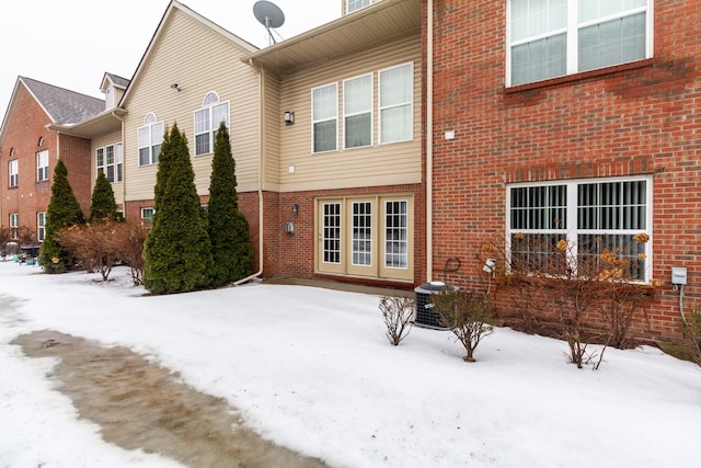 snow covered rear of property featuring central AC unit