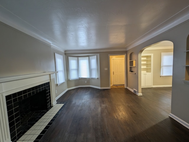 unfurnished living room with crown molding, built in features, dark wood-type flooring, and a tile fireplace