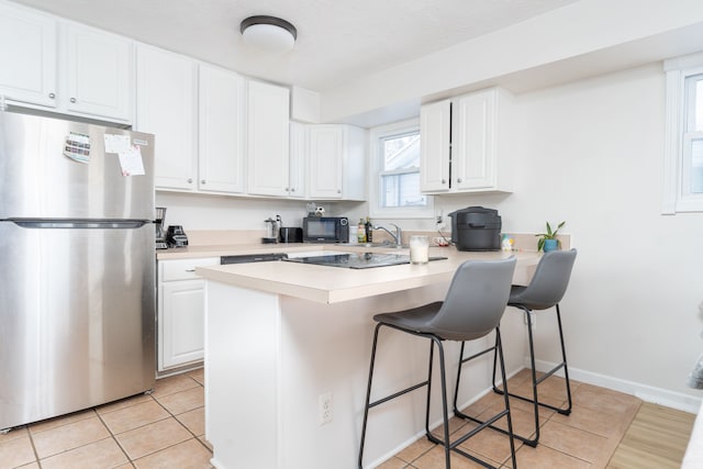 kitchen featuring stainless steel refrigerator, light tile patterned floors, kitchen peninsula, a breakfast bar area, and white cabinets