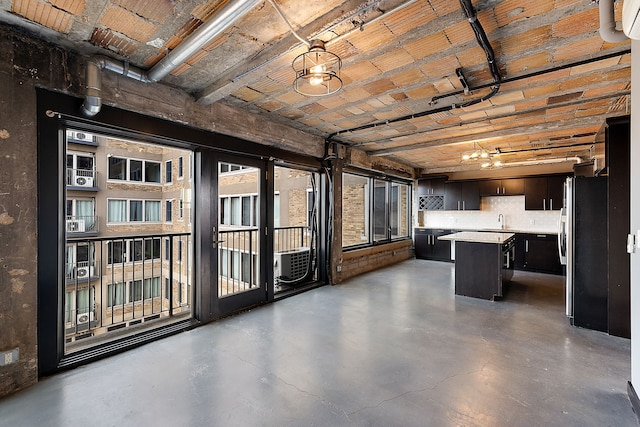 interior space with stainless steel refrigerator, sink, concrete floors, decorative light fixtures, and a kitchen island