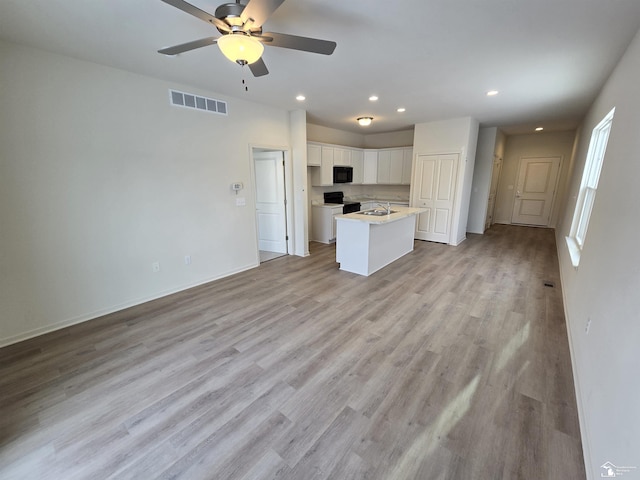 kitchen featuring visible vents, white cabinetry, open floor plan, light countertops, and an island with sink