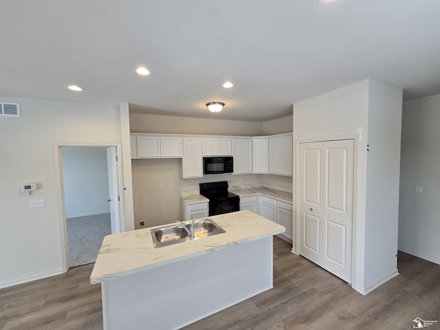 kitchen with a sink, a kitchen island, visible vents, white cabinets, and black appliances