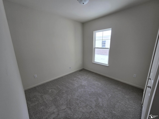 spare room featuring dark colored carpet and baseboards