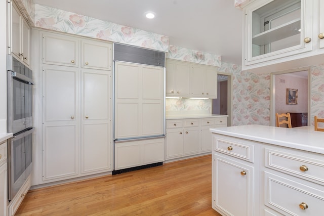 kitchen with paneled fridge, decorative backsplash, light wood-type flooring, and white cabinetry