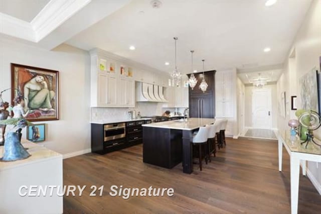 kitchen with a breakfast bar, ventilation hood, dark wood-type flooring, white cabinets, and an island with sink