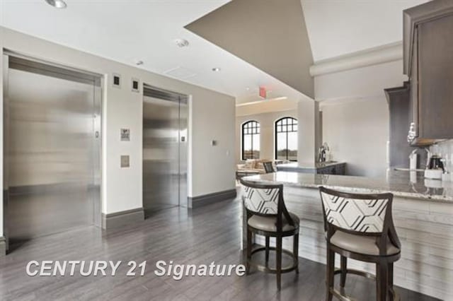 kitchen featuring dark brown cabinetry, light stone countertops, dark wood-type flooring, and elevator