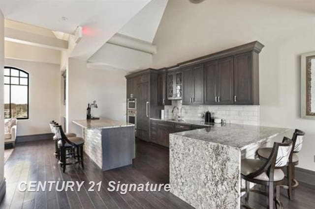 kitchen with a kitchen bar, light stone countertops, dark hardwood / wood-style flooring, tasteful backsplash, and dark brown cabinets